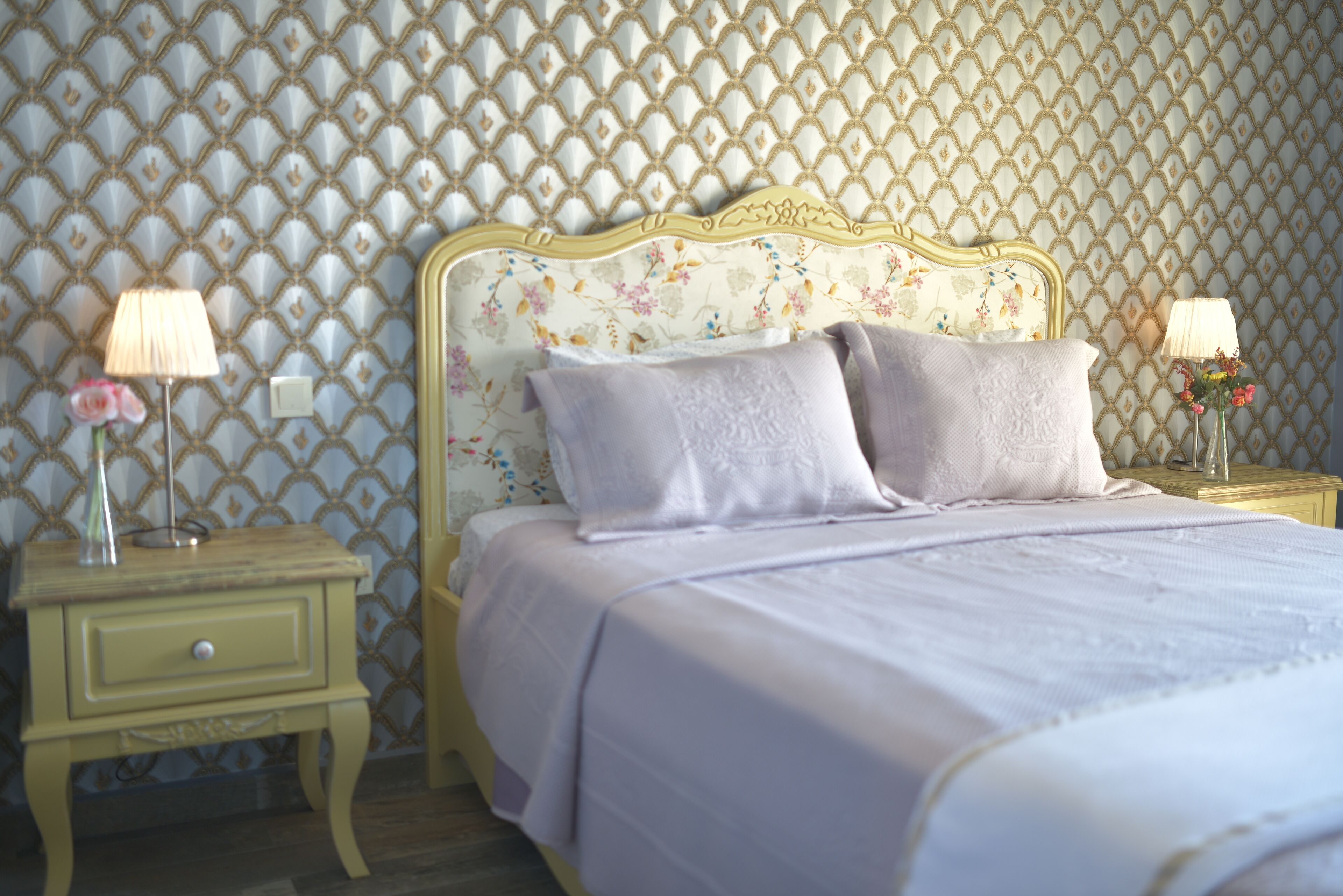A neatly made bed with a floral headboard, two bedside lamps, and a small nightstand with a drawer.