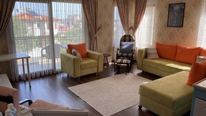 A living room with two sofas, a chair, a small table, and a view of buildings through large windows. - Nilufer Otel - Adult Only (Ayvalik)