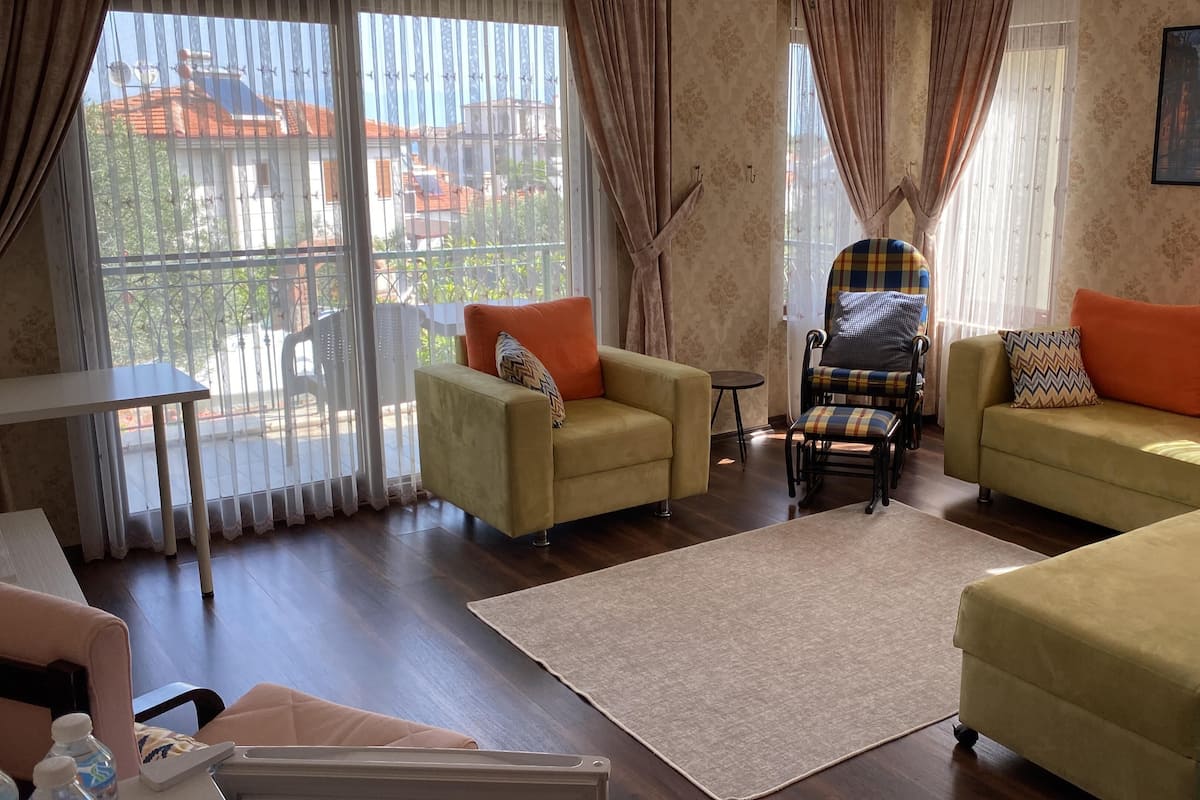 A living room with two sofas, a chair, a small table, and a view of buildings through large windows.