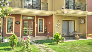 A two-story building with a balcony on the upper floor, a front door, and a small garden area with potted plants. - Nilufer Otel - Adult Only (Ayvalik)