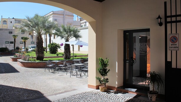 An outdoor patio area with tables and chairs, palm trees, and a building entrance.