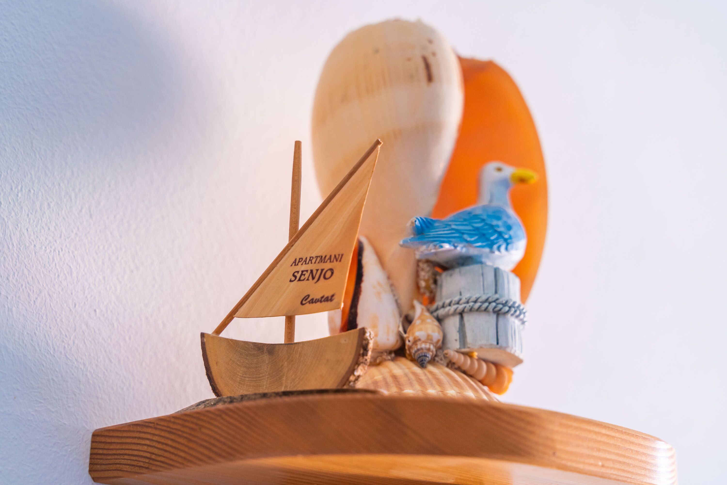 A wooden ship model with a sail labeled "APARTMANI SENJO" and a seagull figurine.