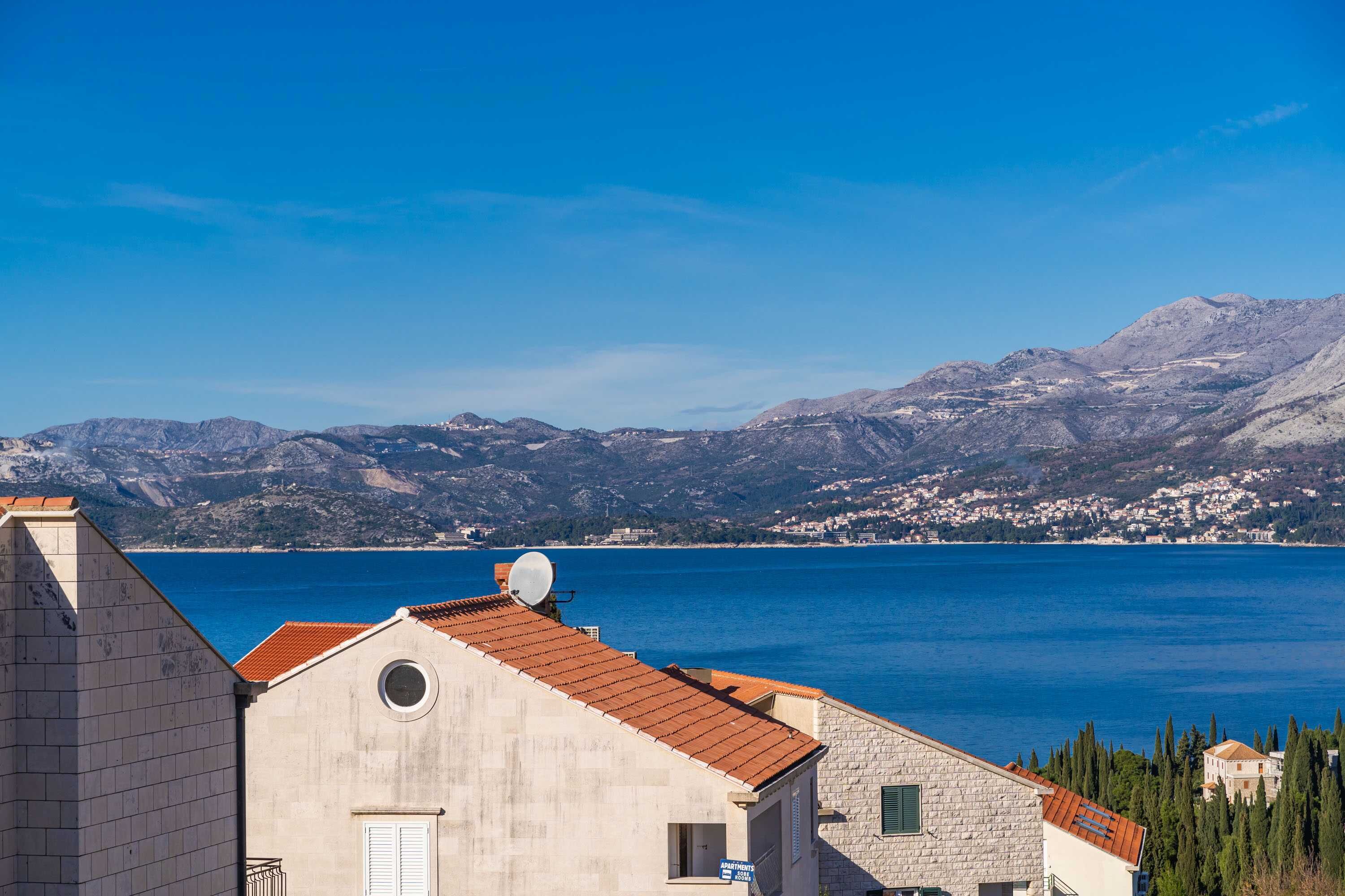 Un bâtiment situé sur la côte, doté d’une façade en pierre, d’une antenne parabolique et offrant une vue sur la mer et les montagnes.