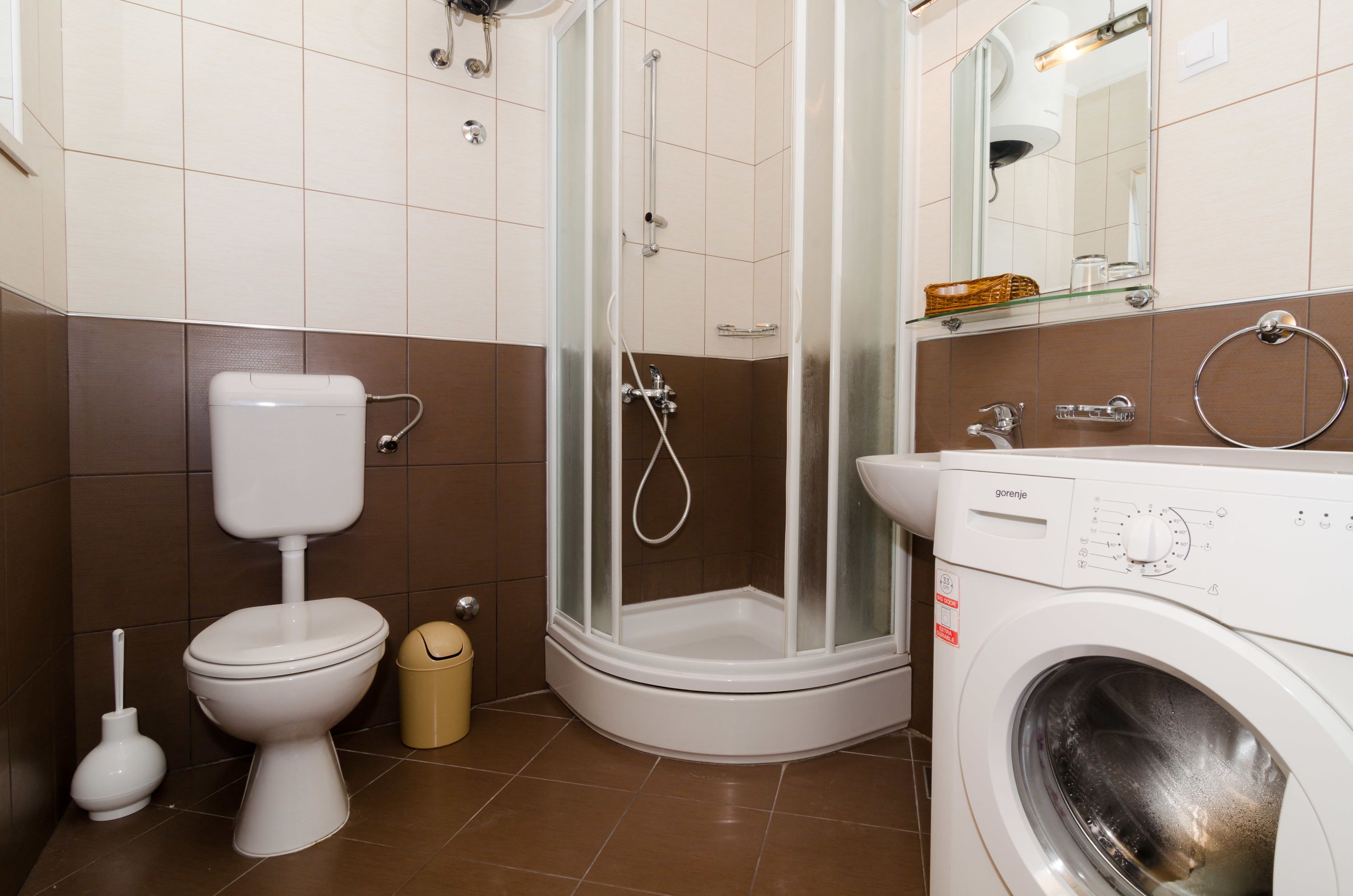 A bathroom with a toilet, a washing machine, and a glass-enclosed shower.