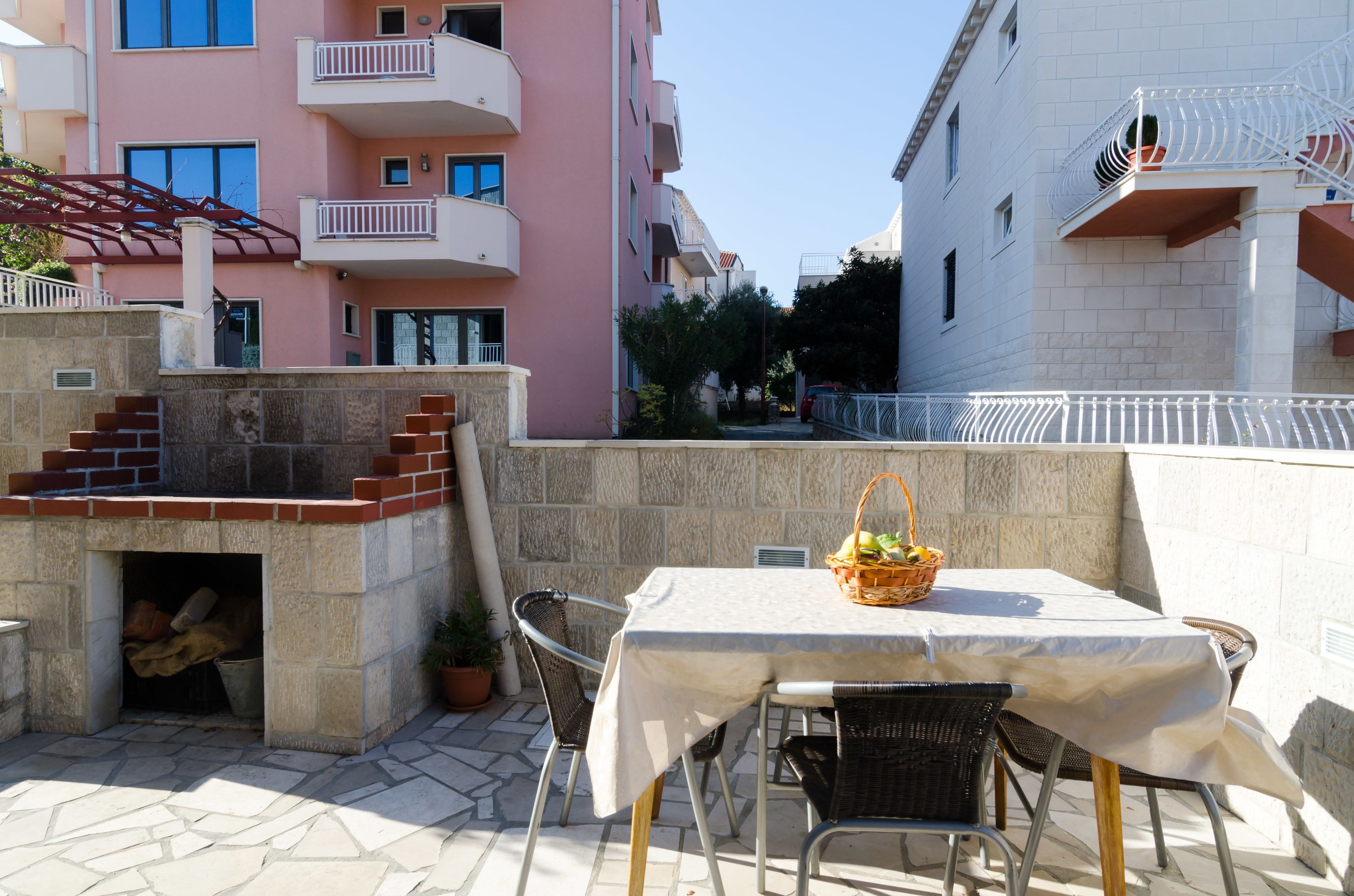 An outdoor patio with a table and chairs, a stone wall, and a pink building in the background.
