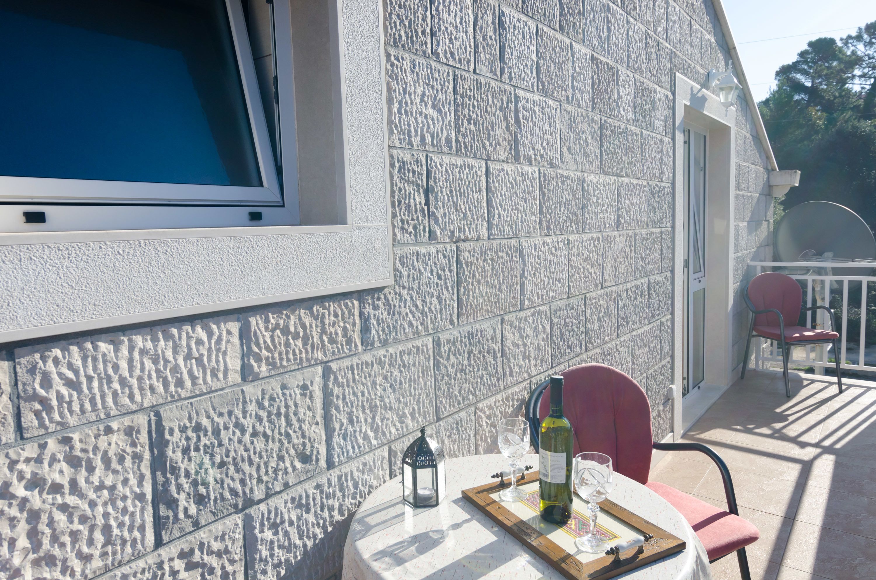 A terrace with a stone wall, a table with a bottle and glasses, and two chairs.