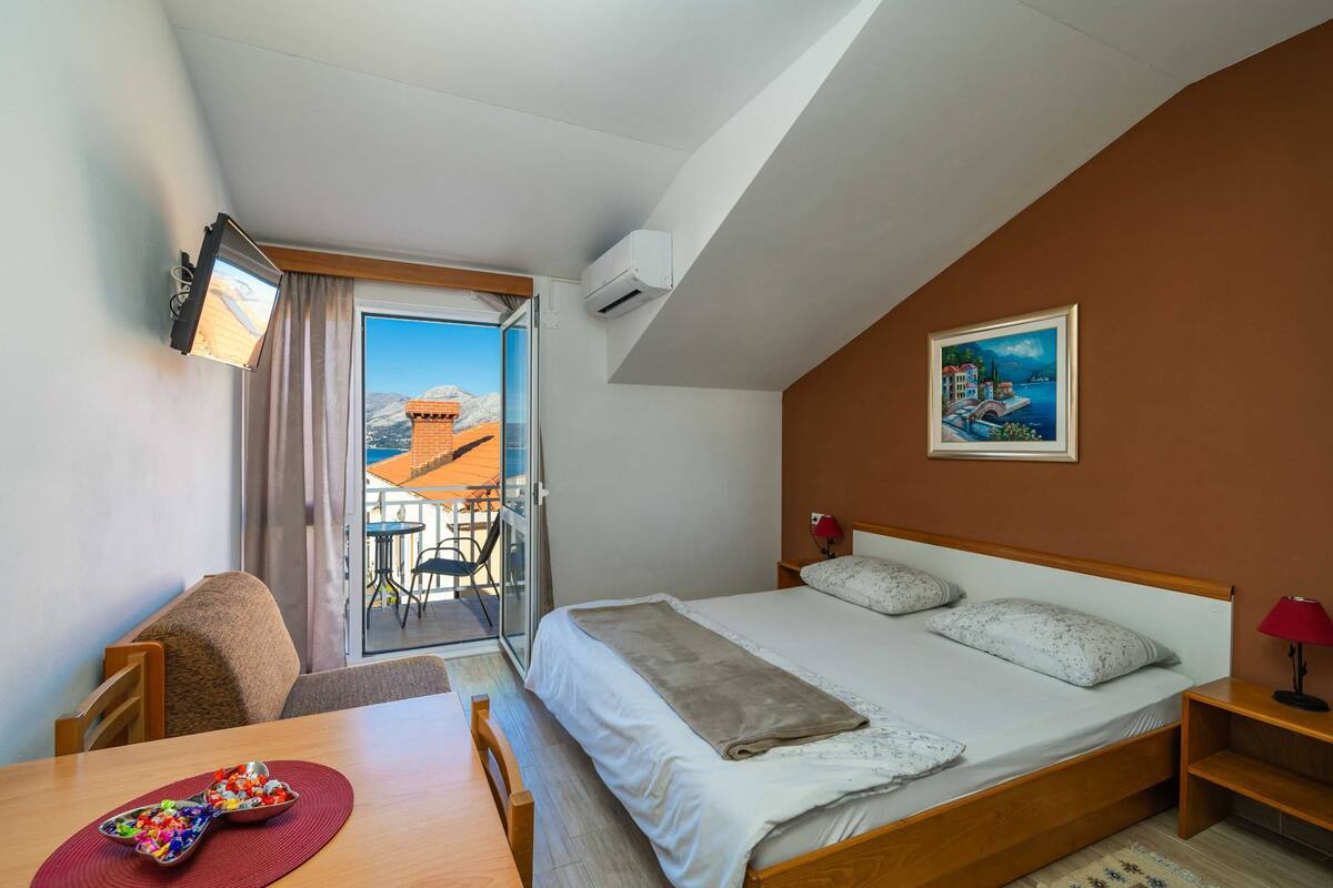 A hotel room with a bed, a desk, a chair, a TV, and a painting on the wall.