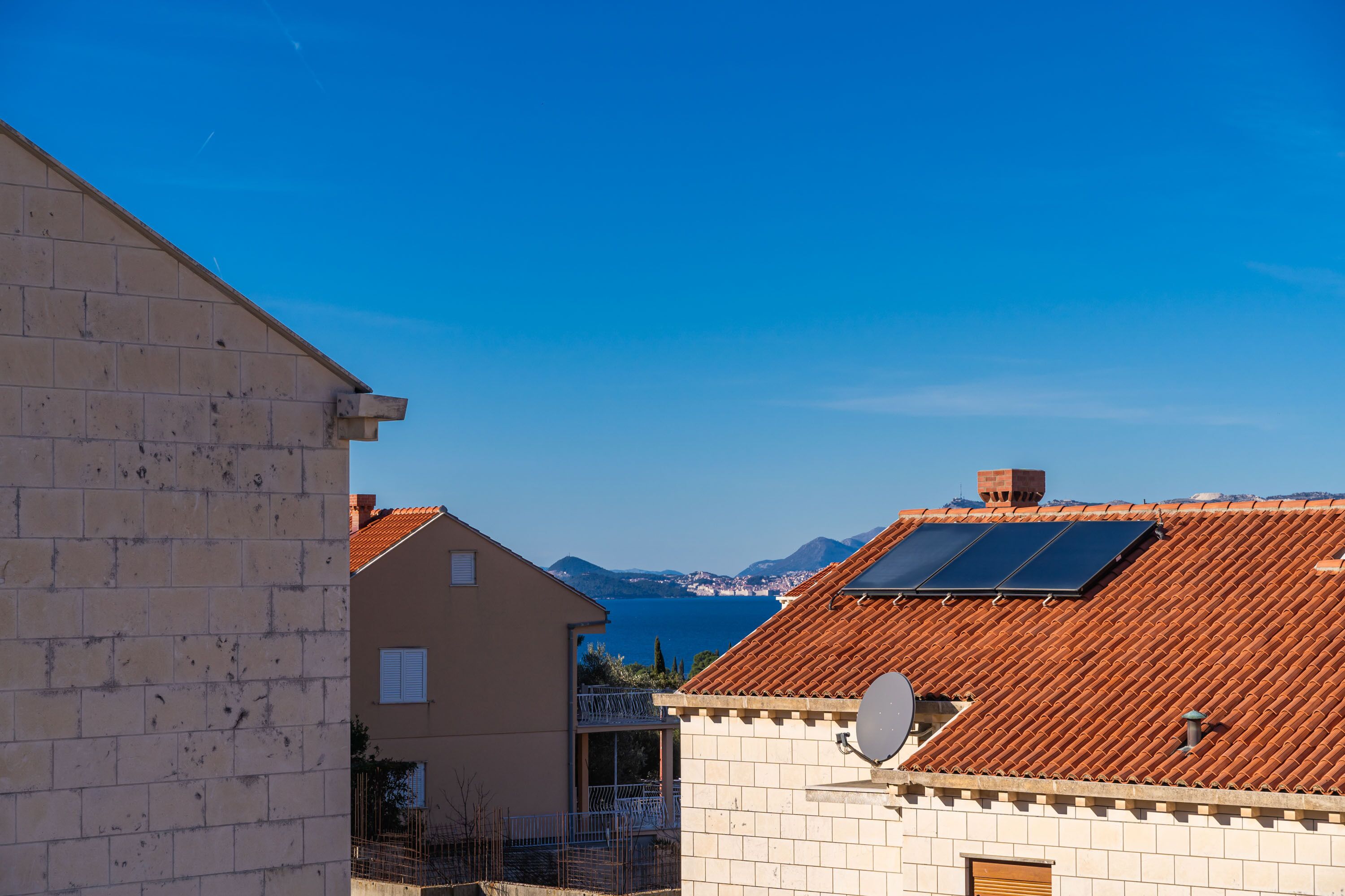 En boligbygning med tegltag, parabolantenne og hav- samt bjergudsigt i baggrunden.