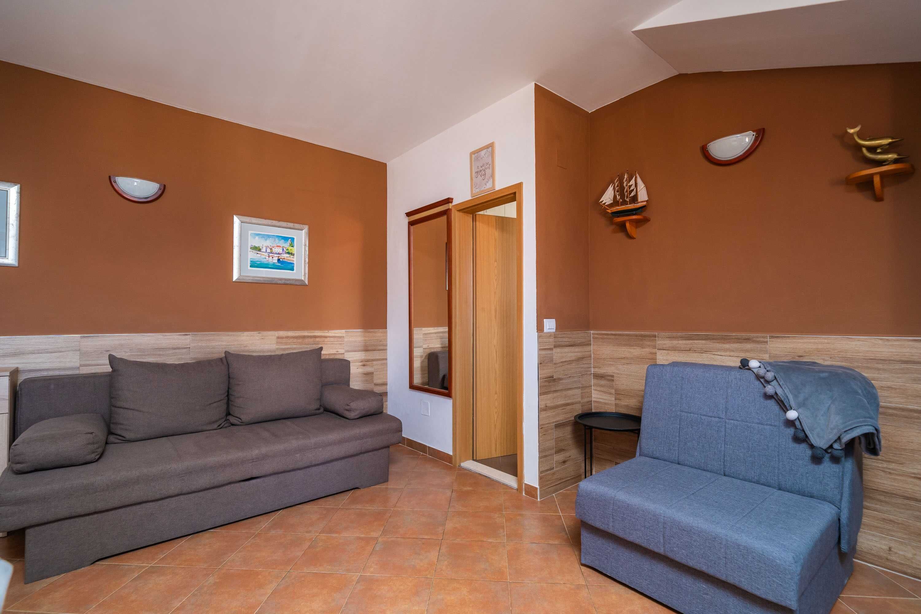 A room with a grey sofa and a blue armchair, a wooden door, and wall-mounted decorative items.