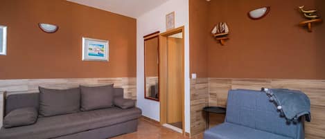 Ein Zimmer mit einem grauen Sofa, einem blauen Sessel, einer Holztür und an der Wand befestigten Dekorationselementen.