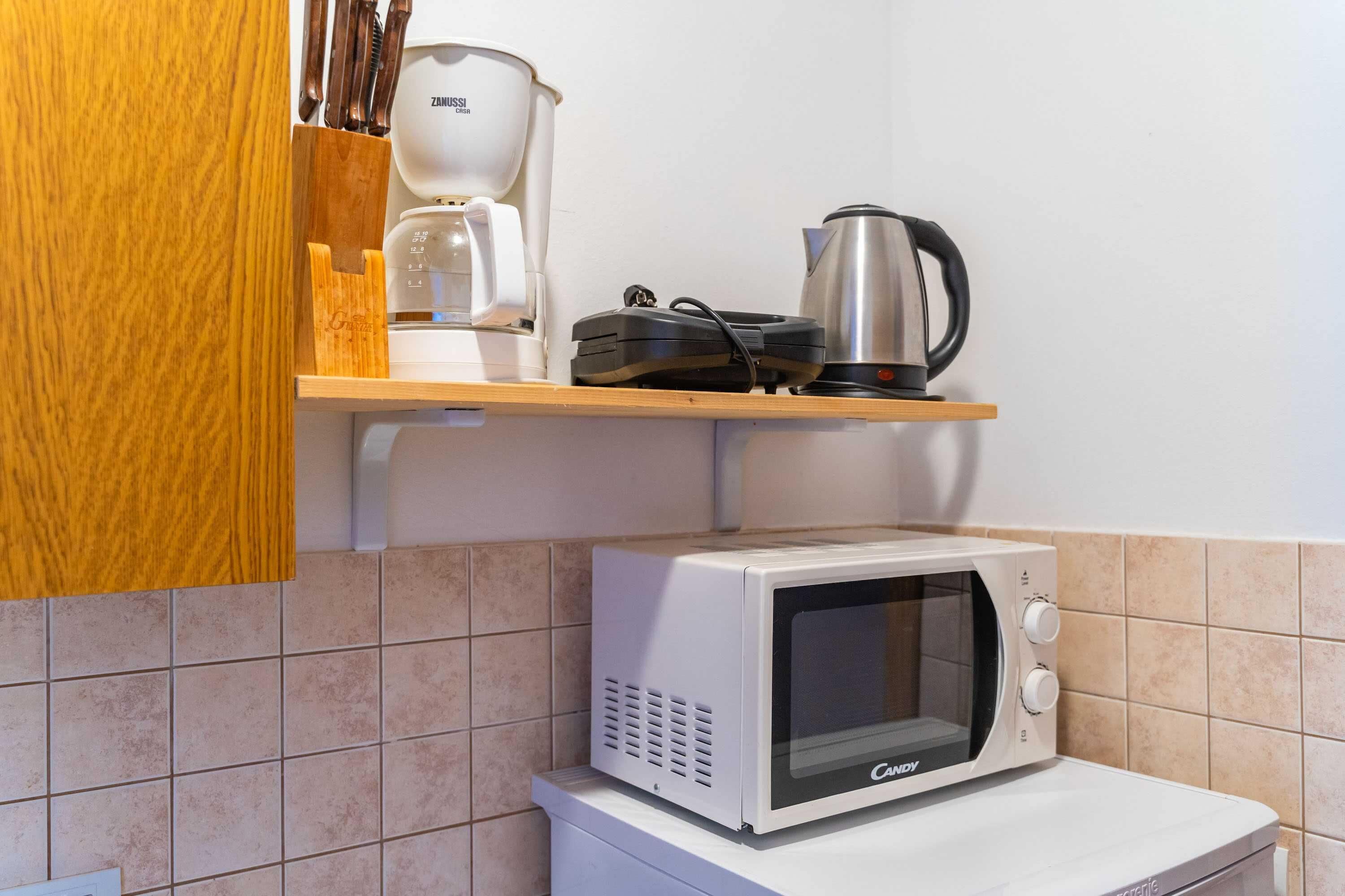 Een keuken met een magnetron, koffiezetapparaat en waterkoker op een plank.