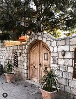 Una entrada de muro de piedra con doble puerta de madera, plantas en macetas y un arco de piedra.