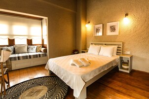 Un dormitorio acogedor con una cama grande, un banco con cojines y una mesita.