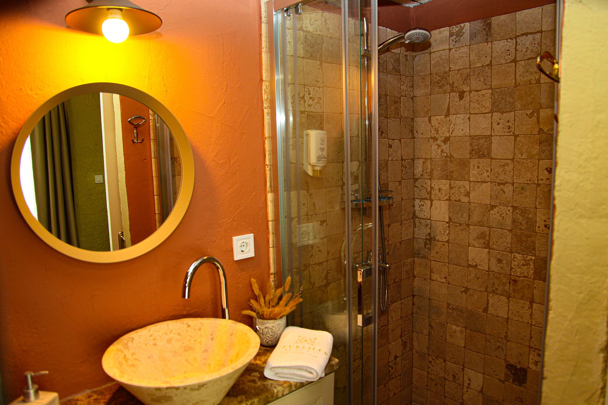 A bathroom with a round mirror, a sink, and a glass-enclosed shower.
