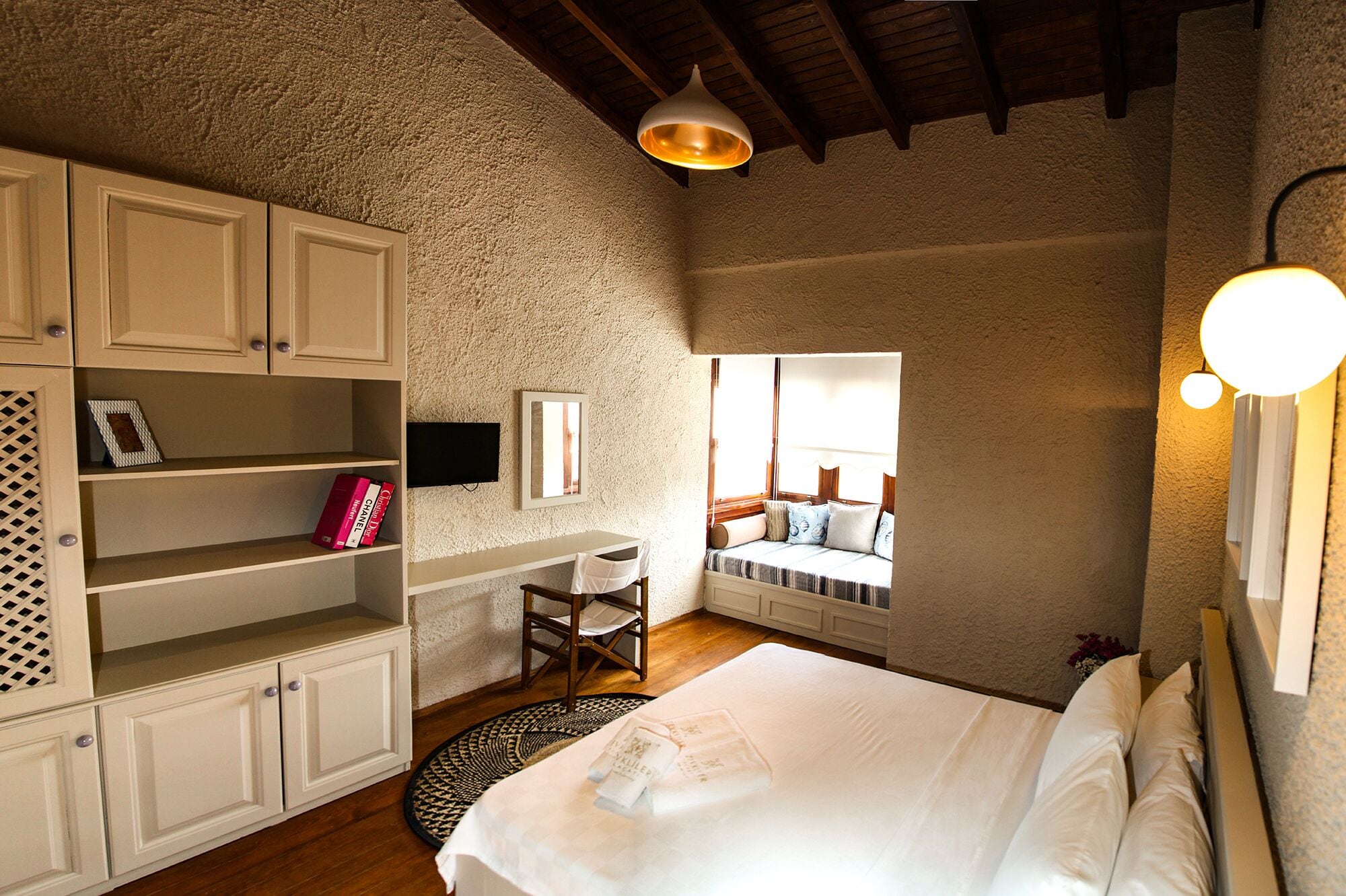 Een slaapkamer met een bed, een bureau, een stoel, een televisie en een raam met uitzicht.