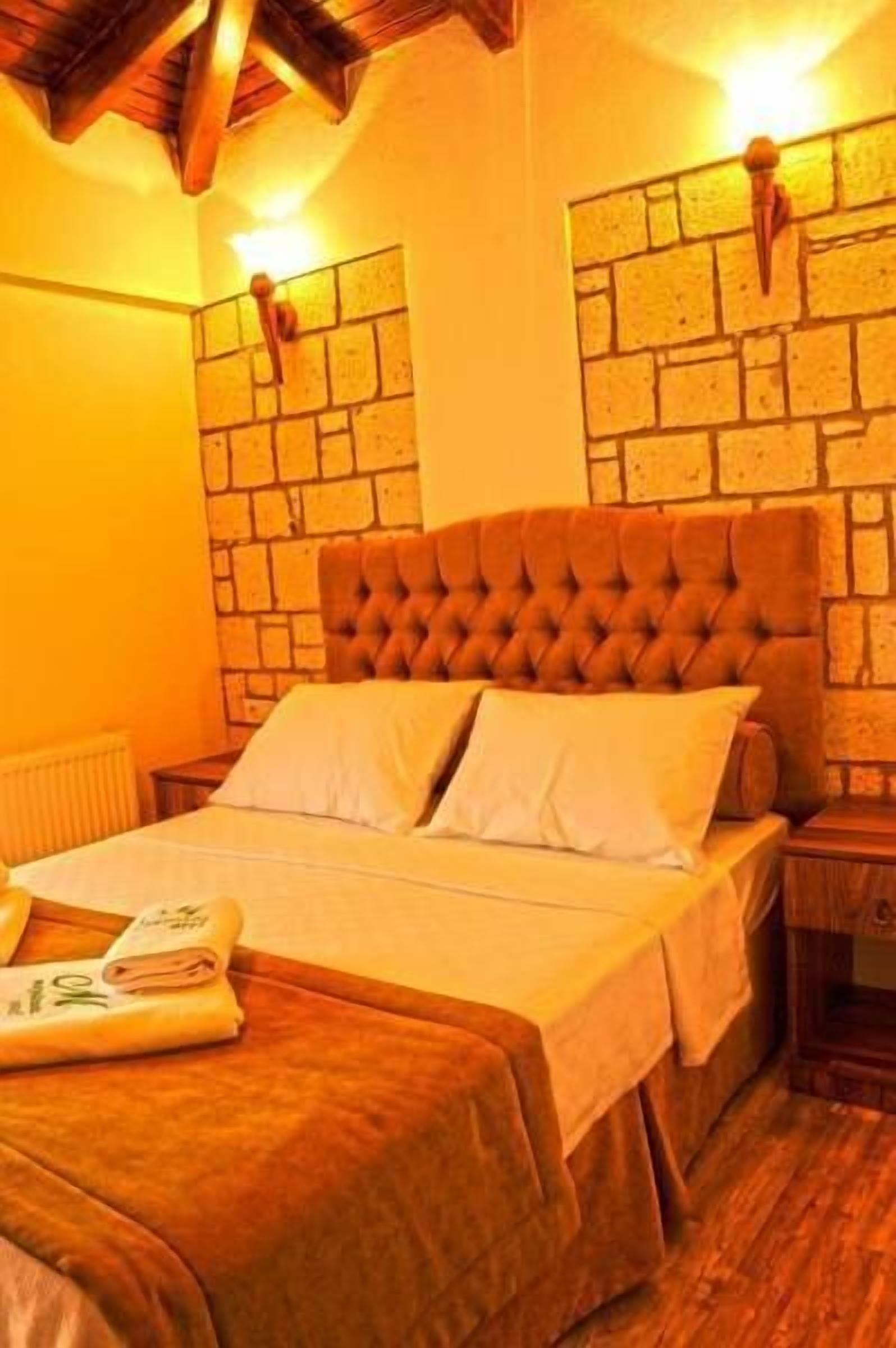 Un dormitorio con cabecera de madera, pared con diseño de ladrillo y cama con ropa blanca.