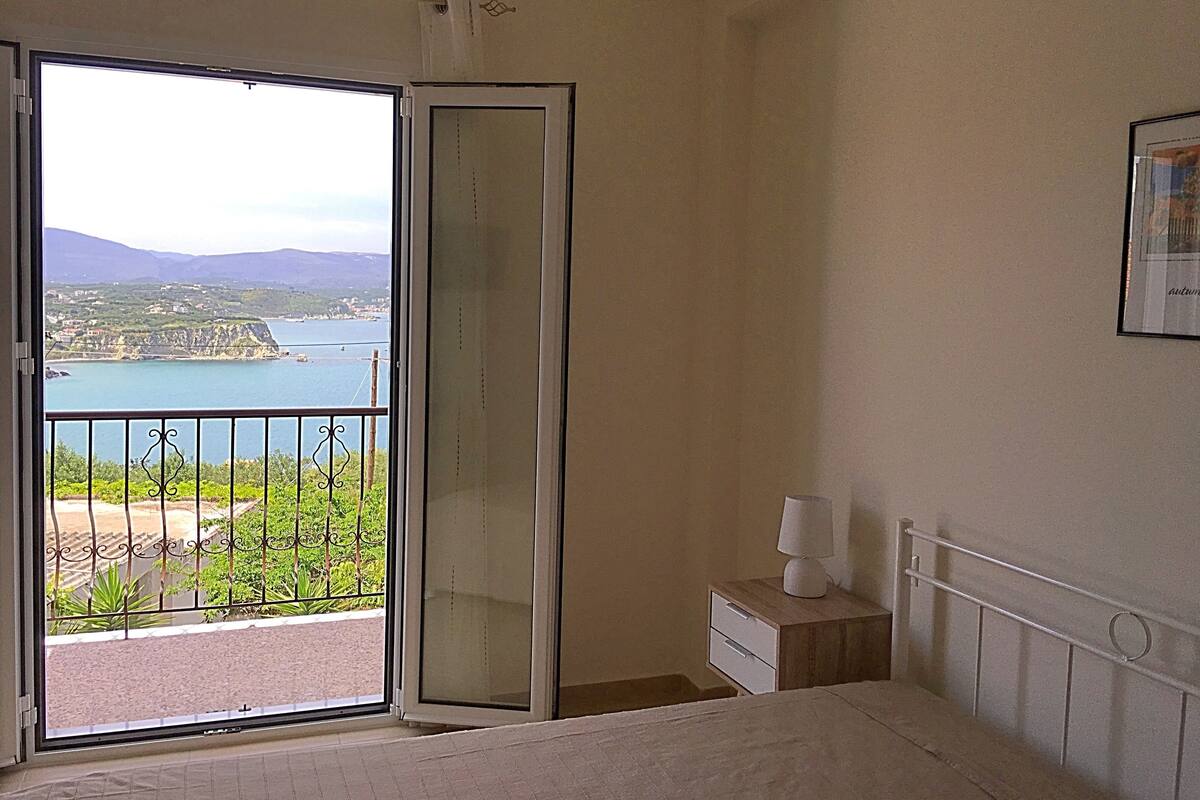 A bedroom with a large sliding glass door leading to a balcony with a view of a coastal area.