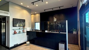 Una moderna zona de recepción de hotel con un mostrador negro, un televisor y un cartel que dice "ATLAS HOTEL".