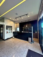 Uma área de recepção de hotel moderna com um balcão preto, uma televisão e uma placa com a inscrição 'ATLAS HOTEL'.