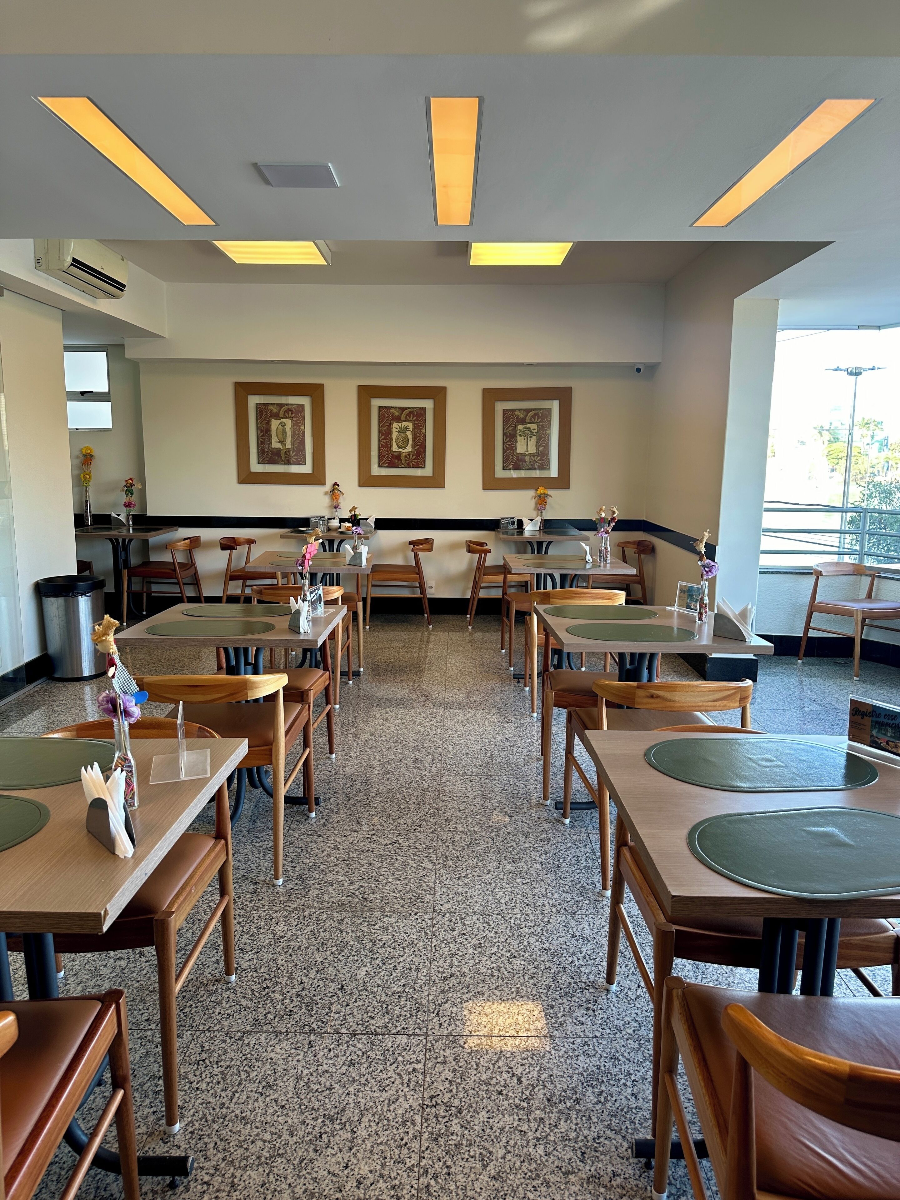 Un restaurante con varias mesas y sillas, obras de arte en las paredes y vistas al exterior a través de amplias ventanas.