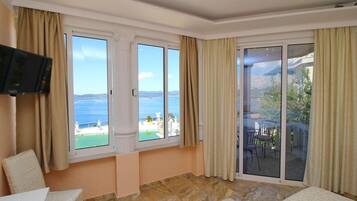 Una habitación con un gran ventanal corredera que da a un balcón con vistas al mar y a las montañas.