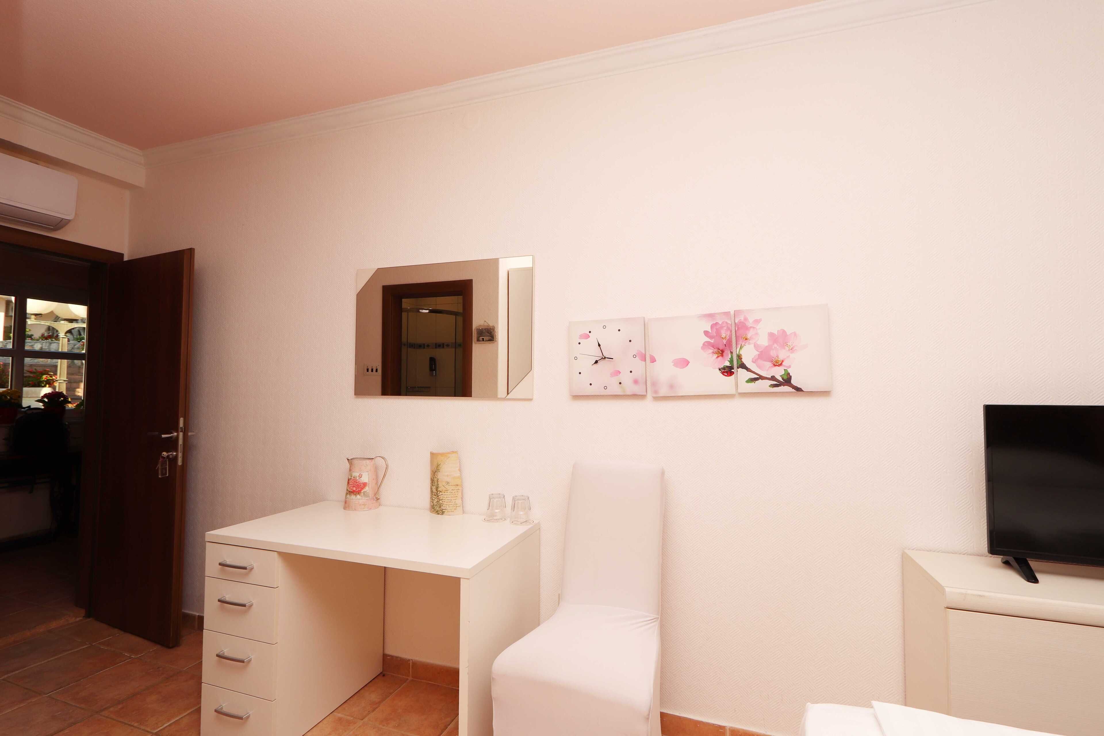 Een slaapkamer met een wit bureau, een stoel, een televisie en kunst aan de muur.