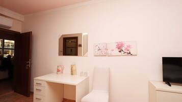 Een slaapkamer met een wit bureau, een stoel, een televisie en kunst aan de muur.