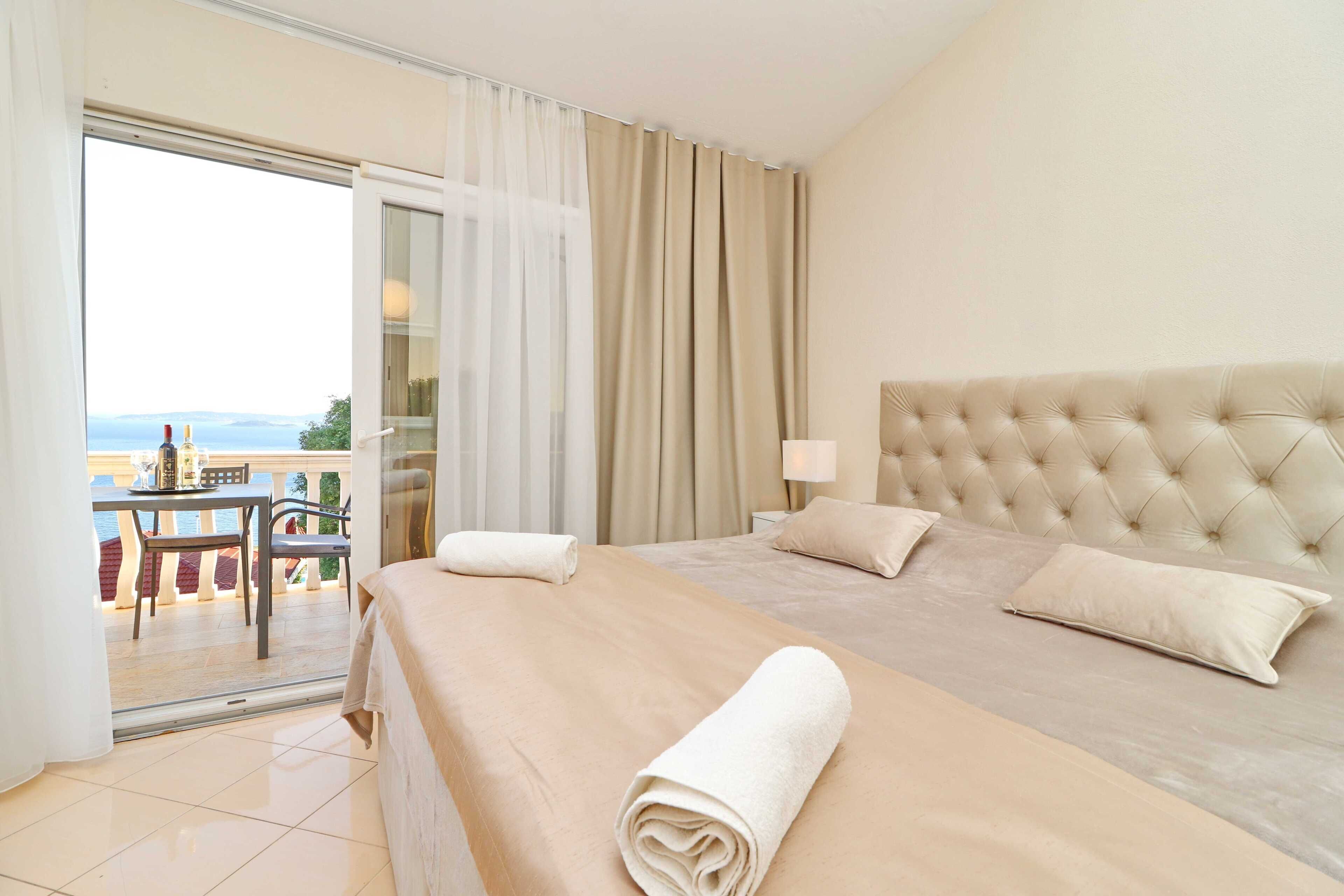 Habitación de hotel con una cama grande, un balcón con mesa y sillas, y vista al mar.