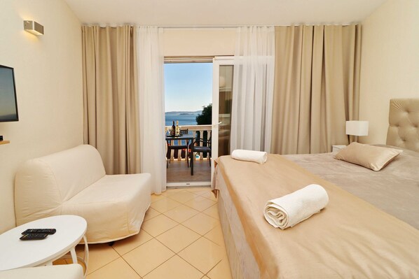 A hotel room with a bed, a sofa, a small table, and a TV. There is a balcony with a table and chairs outside. - Villa Antonio (Orebic)