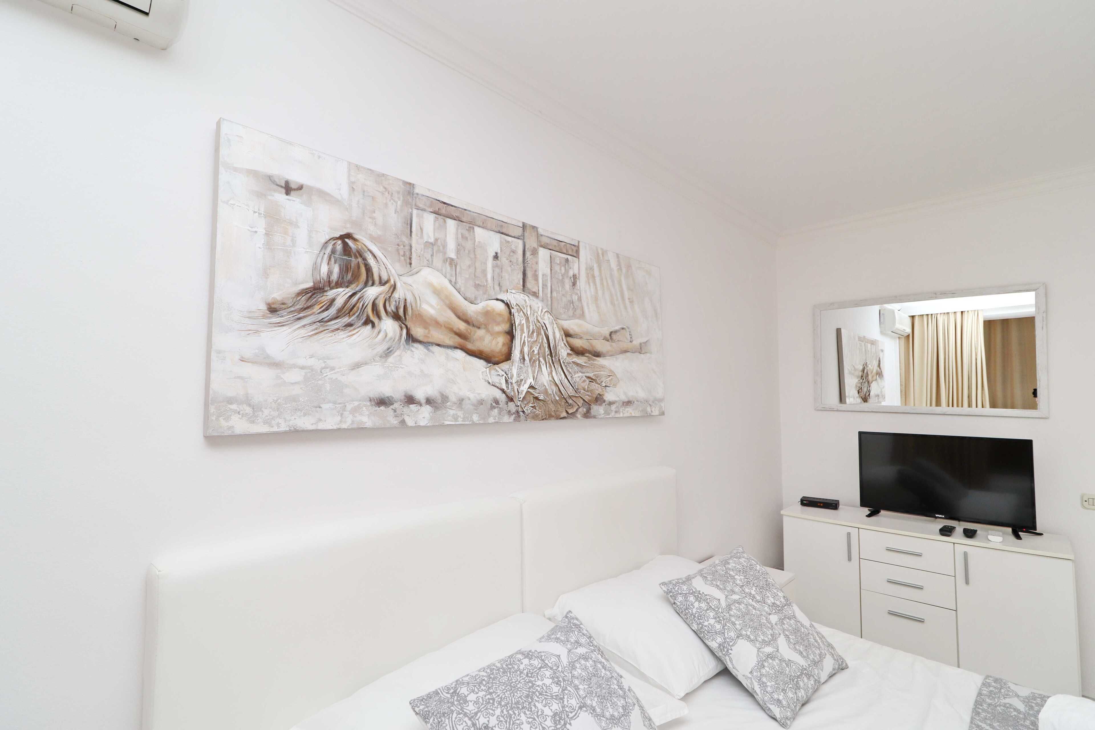 Une chambre avec un grand tableau, une télévision et un lit agrémenté d’oreillers à motifs.