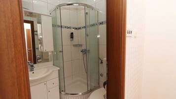 Un baño moderno con ducha envuelta en vidrio, un lavamanos blanco y un inodoro.