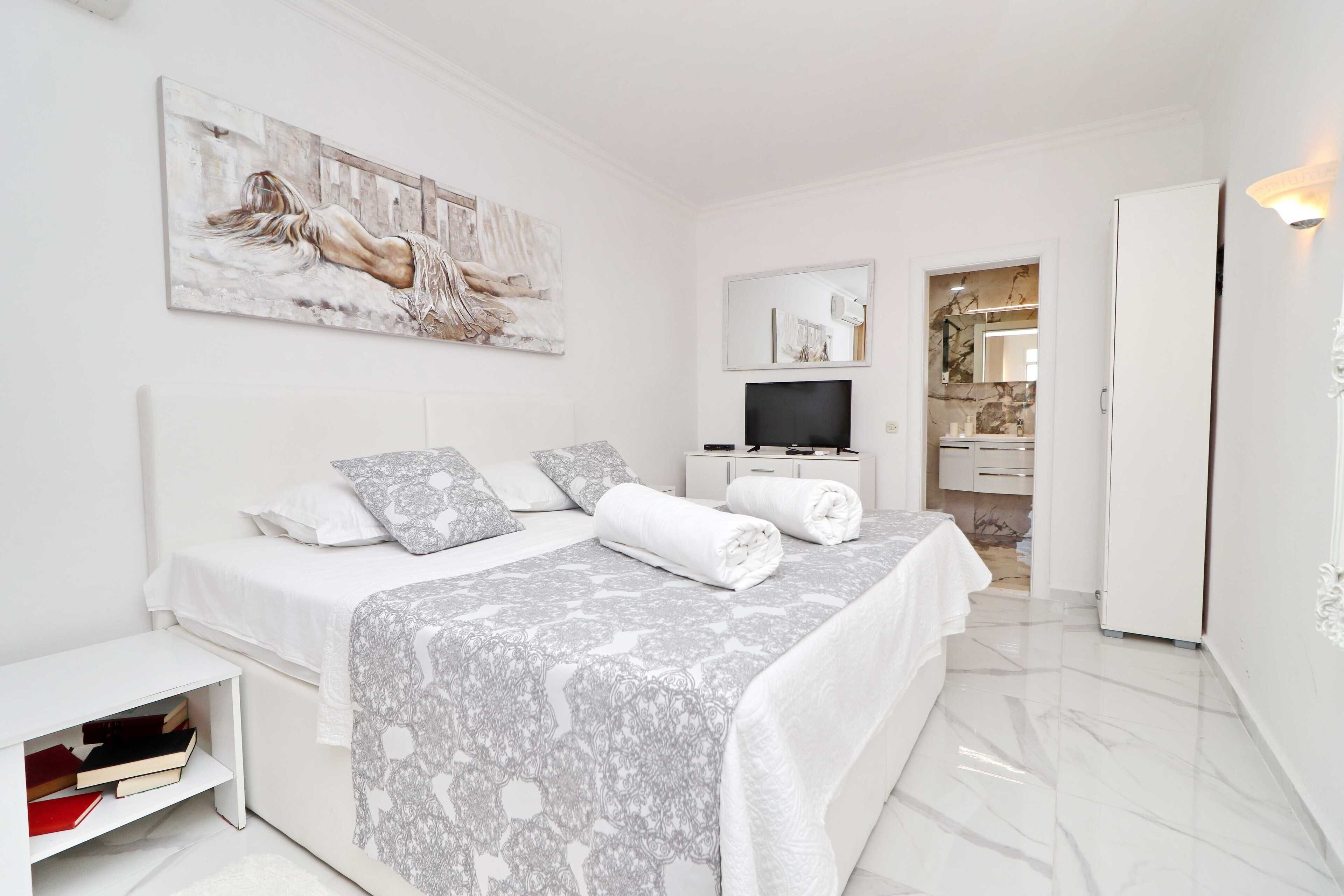 Una camera da letto moderna con un letto grande, una TV e un bagno visibile attraverso una porta aperta.