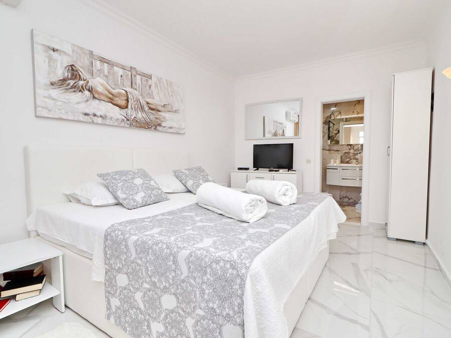 A modern bedroom with a large bed, a TV, and a bathroom visible through an open door.