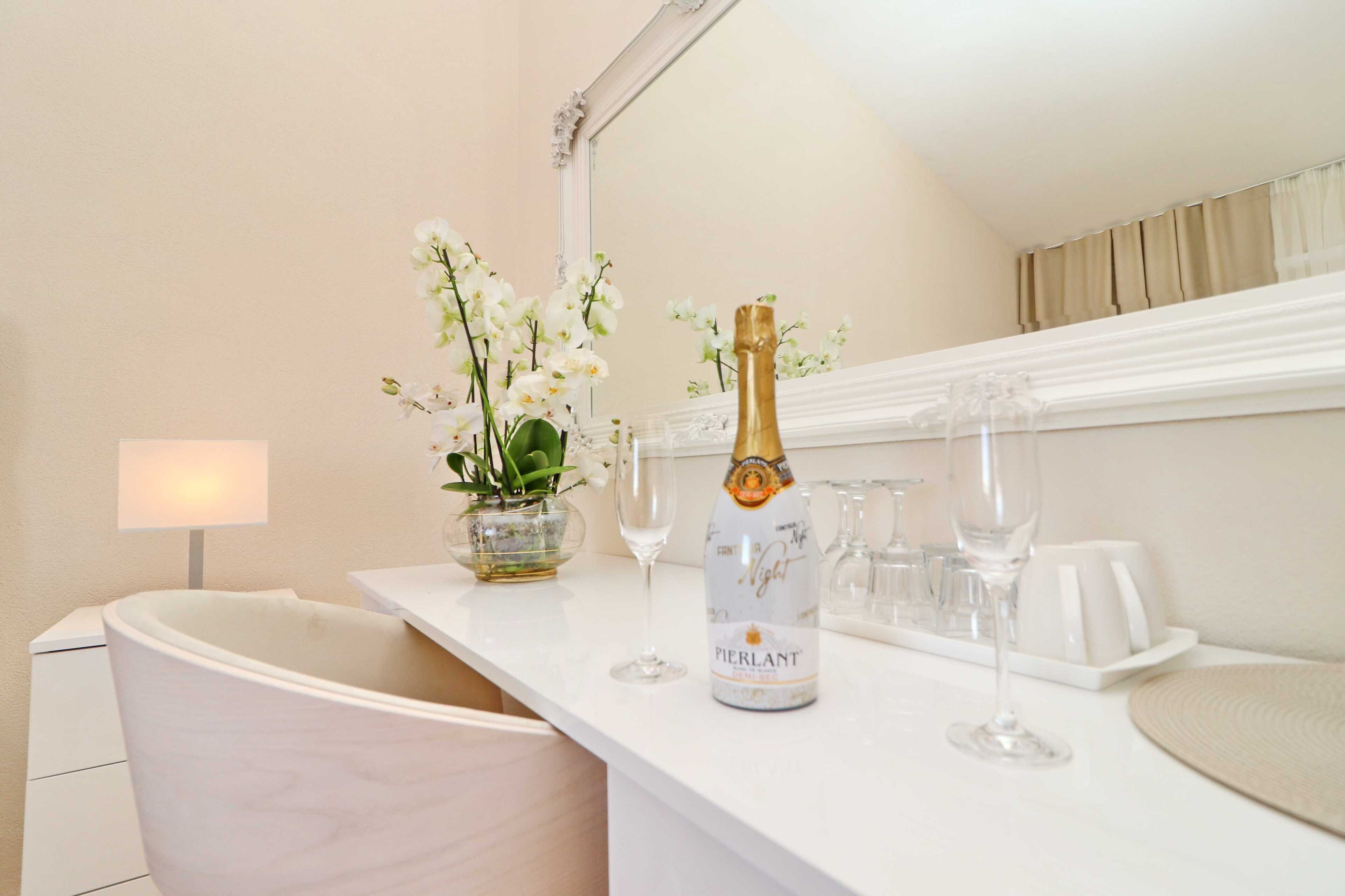 A bathroom vanity with a white marble countertop, a bottle of Pierlant champagne, and a vase of white orchids.