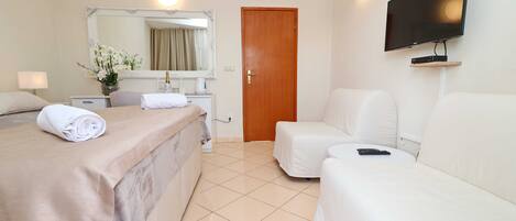 A hotel room with a bed, a sofa, a TV, a mirror, and a door.
