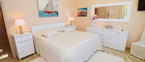 A bedroom with a bed, nightstands, a dresser, a chair, and artwork on the walls.