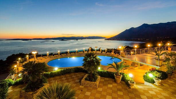 Un espace piscine offrant une vue sur la mer et les montagnes au crépuscule.