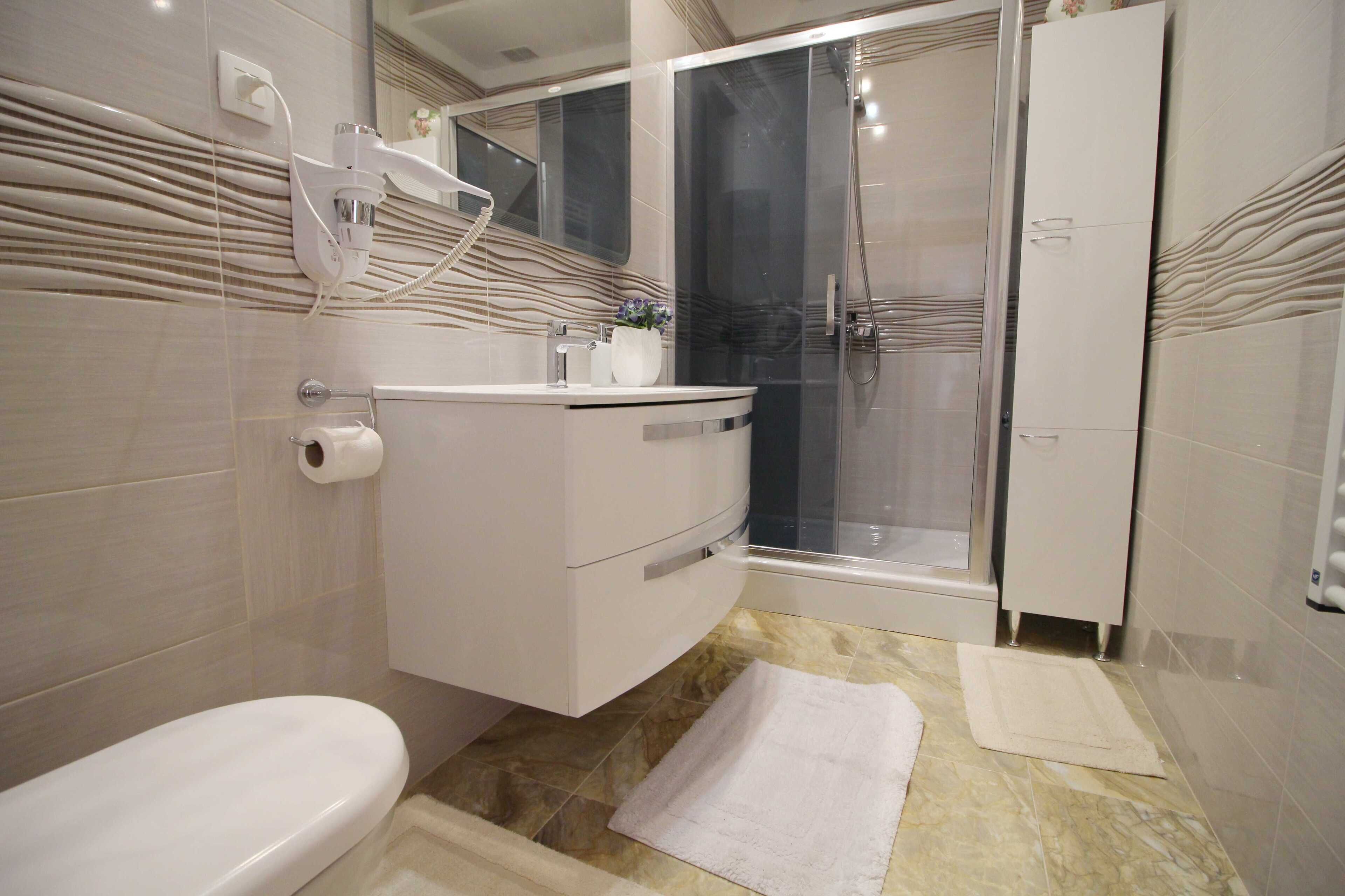 A modern bathroom with a toilet, a sink with a mirror, a shower area, and a cabinet.