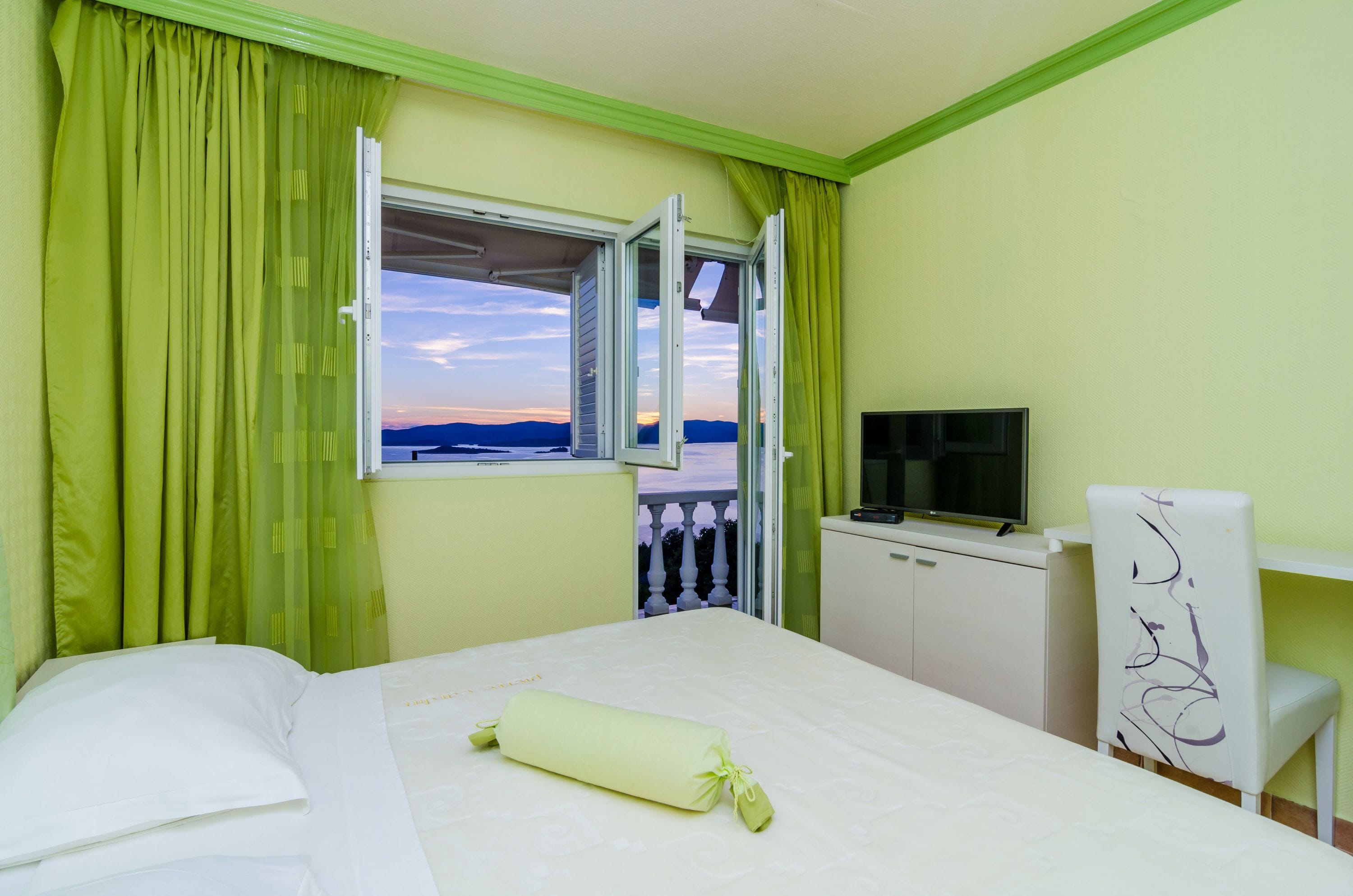 Une chambre d’hôtel avec un lit, une télévision, un bureau et une fenêtre avec des rideaux.