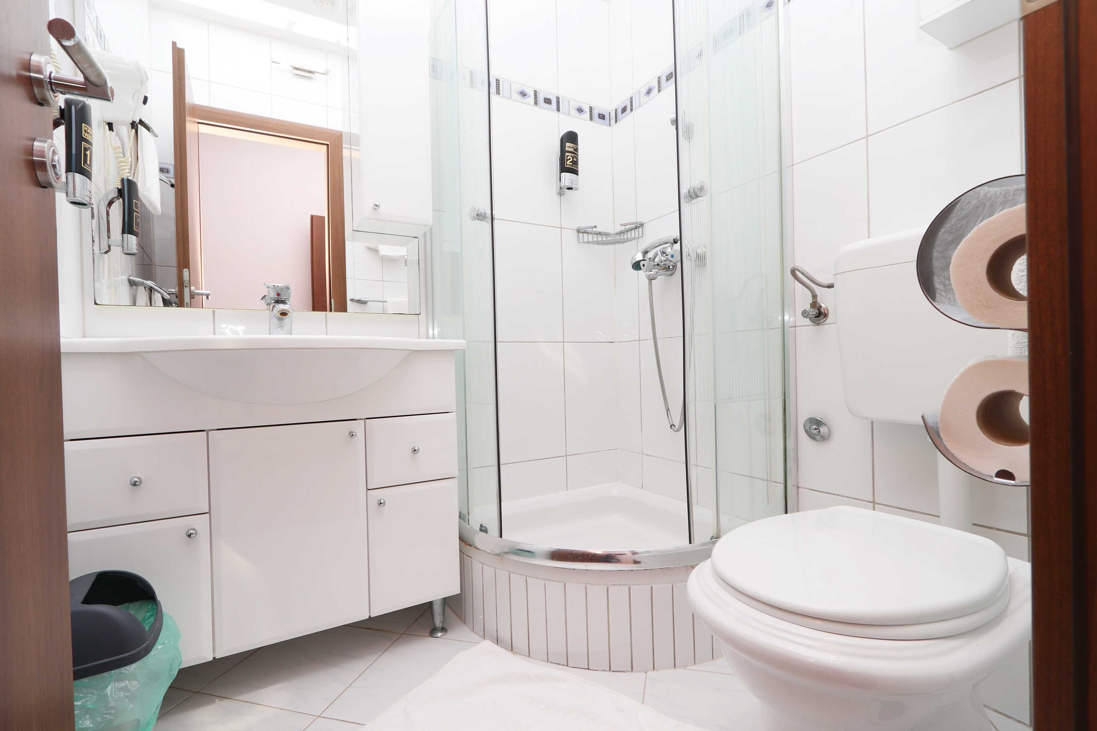 Ein modernes Badezimmer mit einer Duschkabine, einer weißen Toilette und einem Waschtisch mit Spiegel und Handtuchhalter.