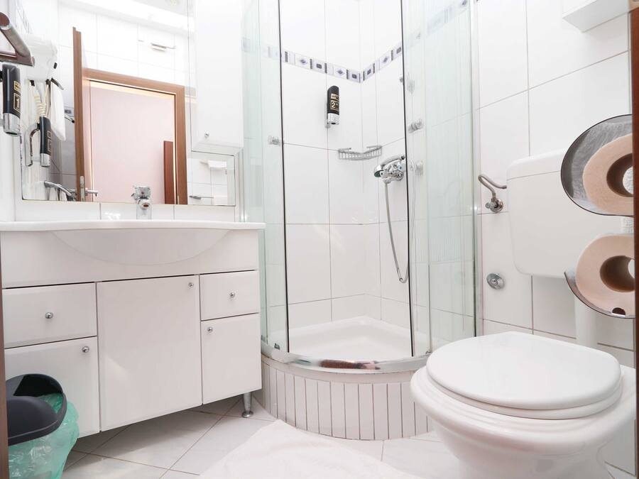 A modern bathroom with a glass-enclosed shower, a white toilet, and a vanity with a mirror and towel rack.