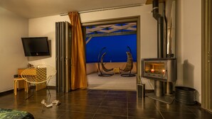 A modern hotel room with a large window, a fireplace, a television, and a comfortable seating area. - Skinos ilivatos Boutique Eco Villa (Kefalonia)
