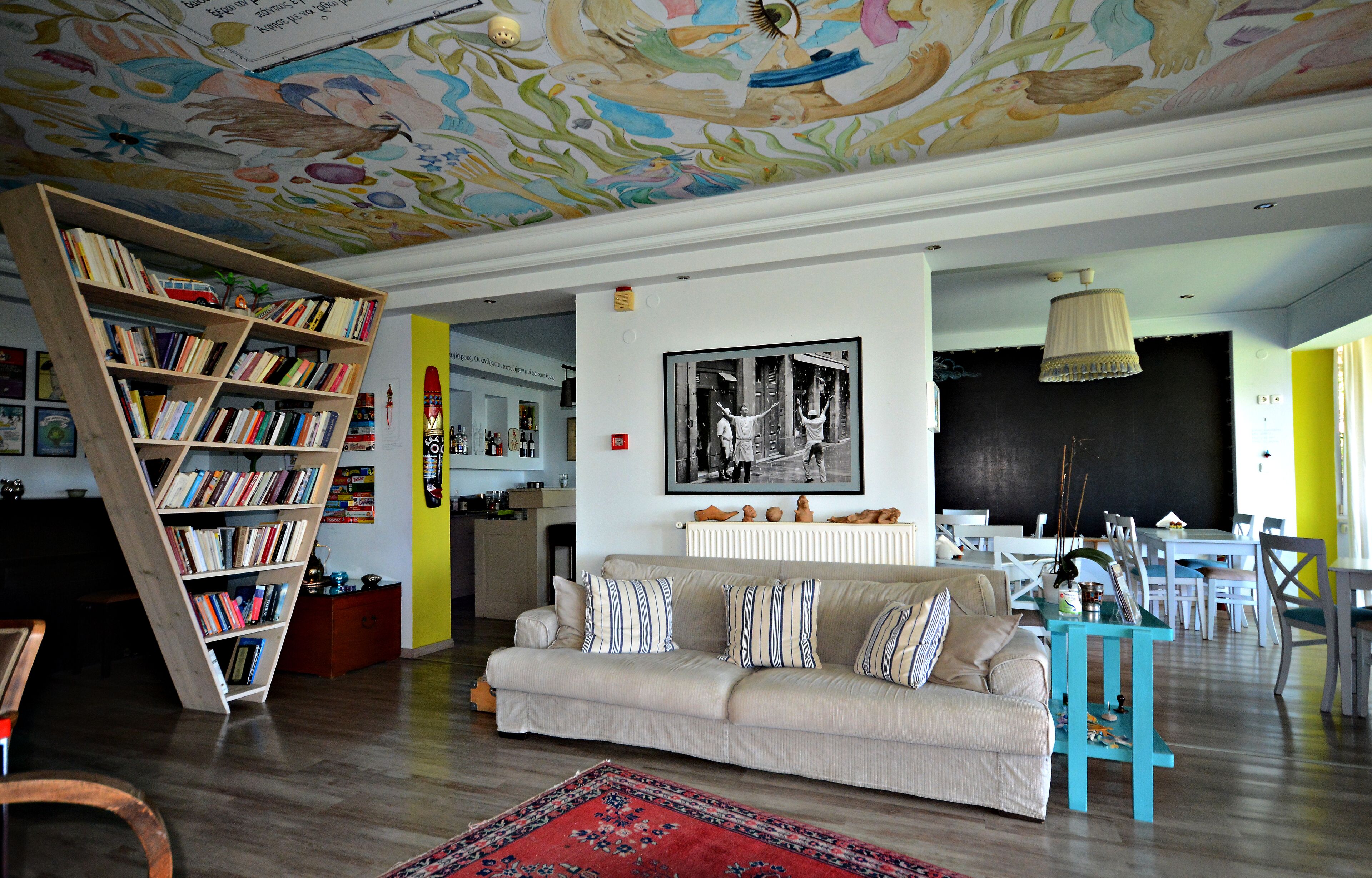 Una sala de estar con sofá, estantería, comedor y un mural en el techo.