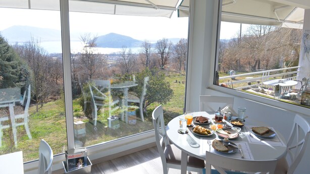 A dining area with a table set for two, overlooking a scenic view of trees and mountains through large windows.