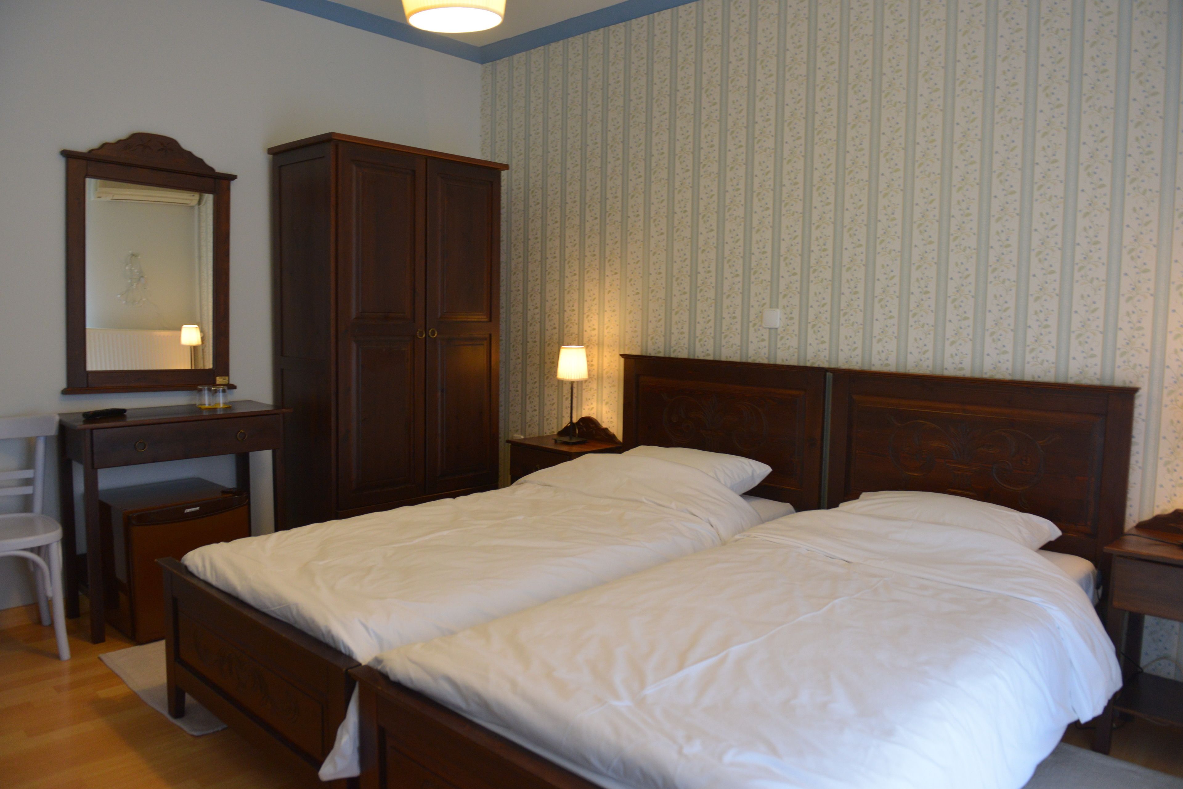 A bedroom with a double bed, a wooden wardrobe, a desk with a chair, and a mirror.