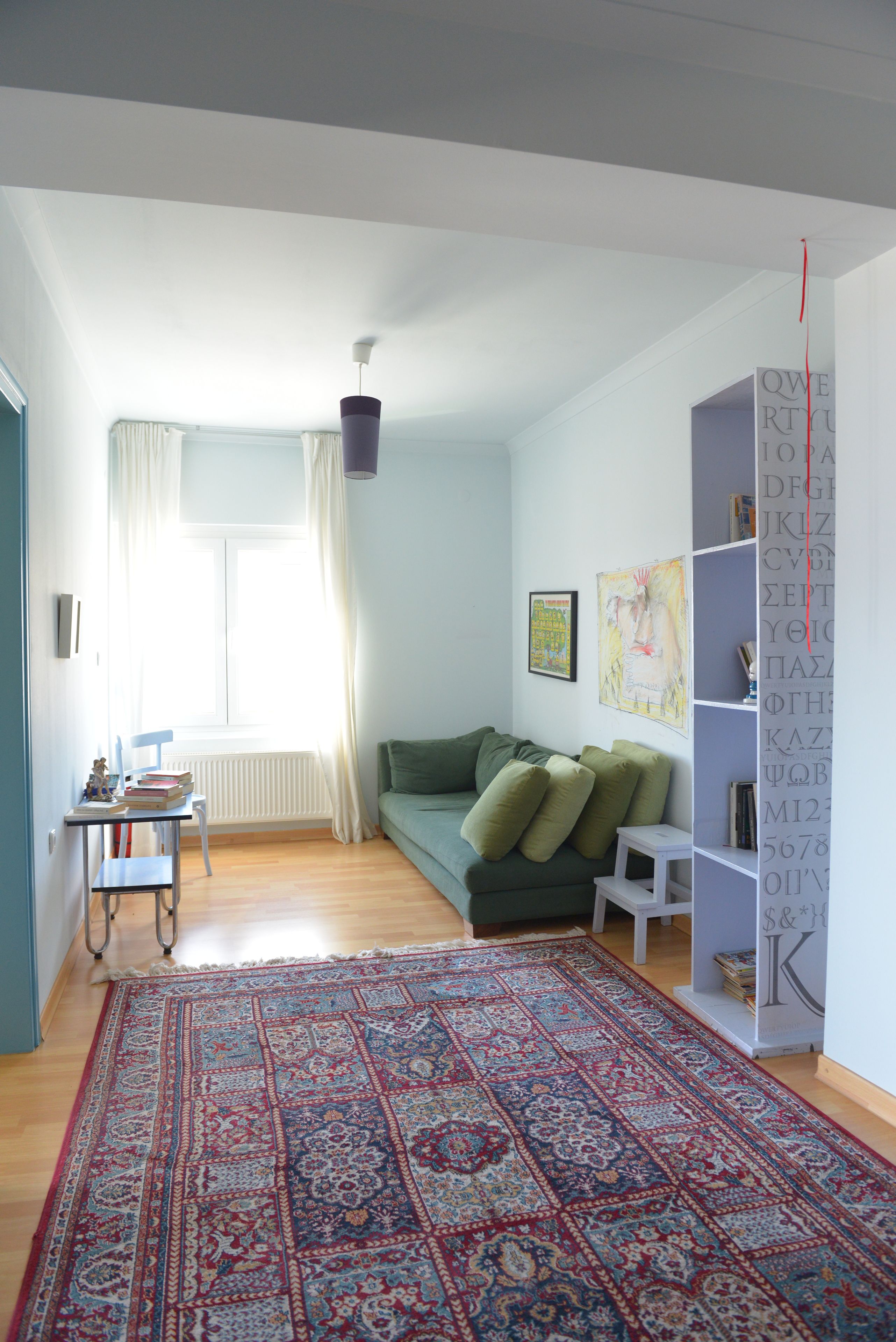 A living room with a green sofa, a patterned rug, a white radiator, and a bookshelf.