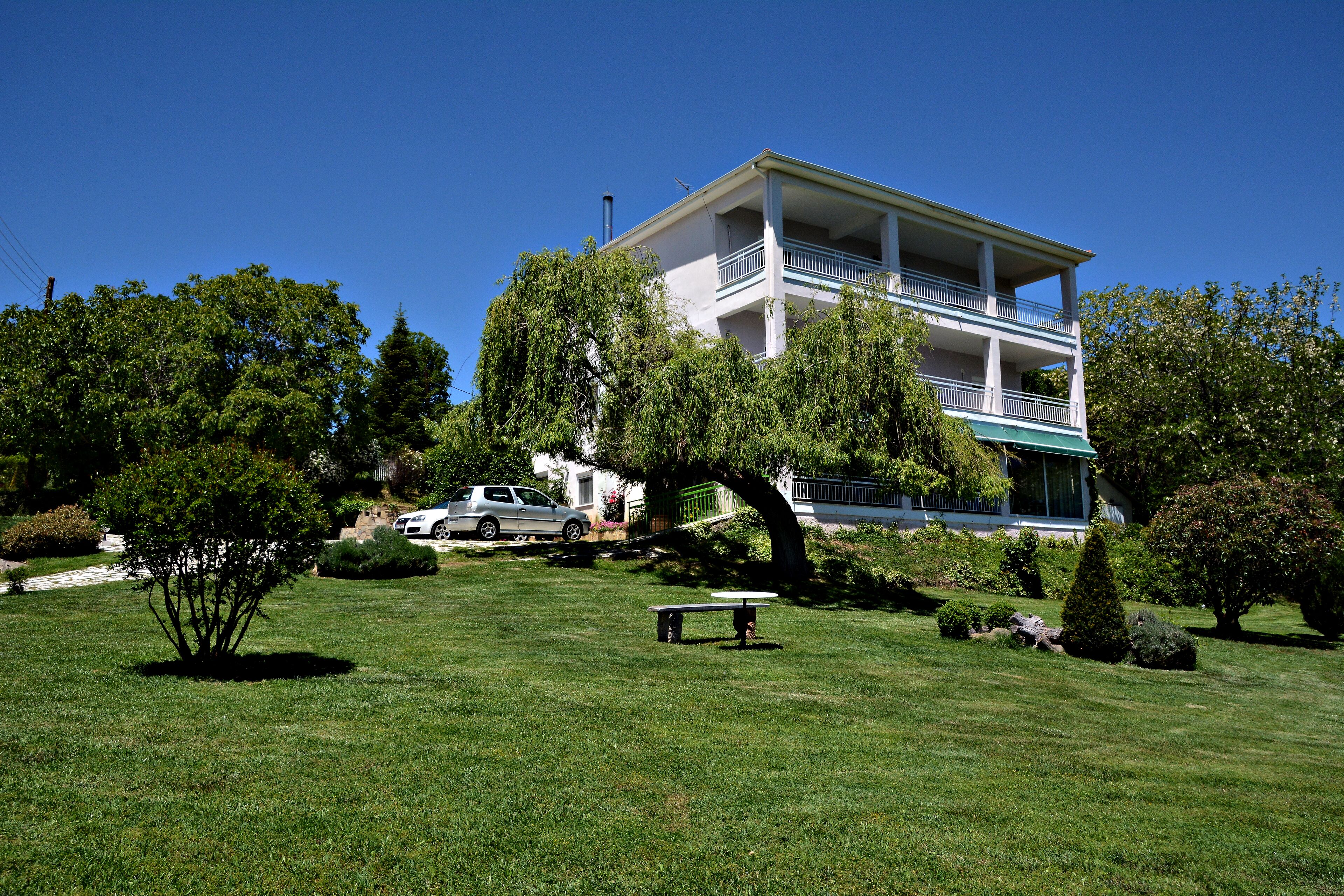 A two-story building with a balcony, surrounded by a well-maintained lawn and trees.