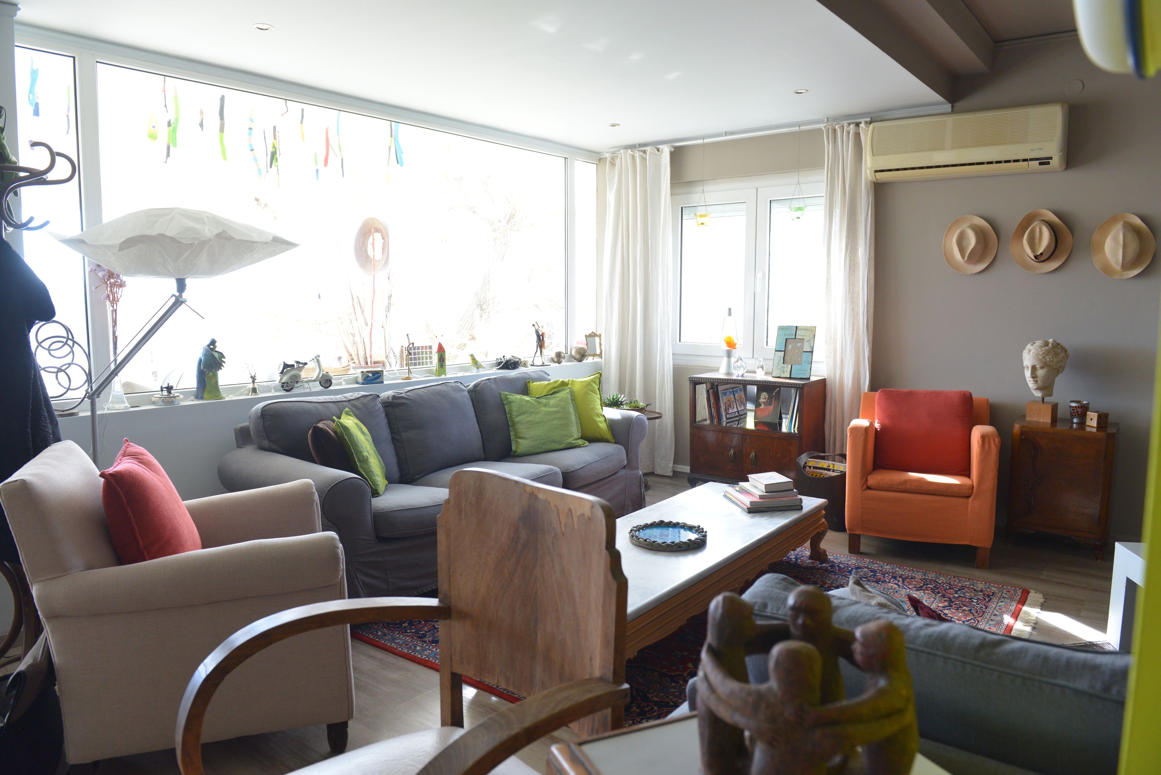 A living room with a sofa, armchairs, a coffee table, and a side table. There is a window with curtains, a wall-mounted air conditioner, and a small statue on the side table.