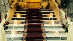 Una imponente escalera con alfombra roja, paredes de piedra y faroles en cada peldaño.