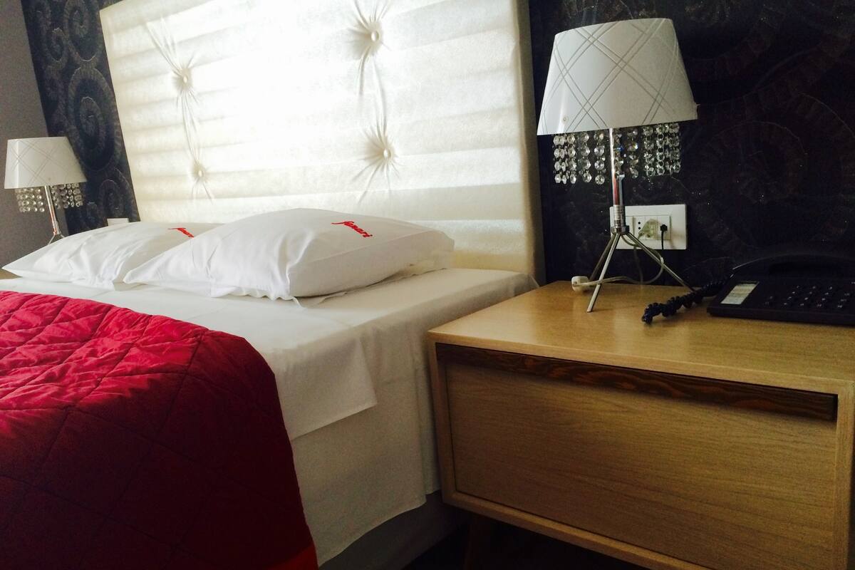 A hotel room with a bed, a bedside table with a lamp, and a desk with a phone.